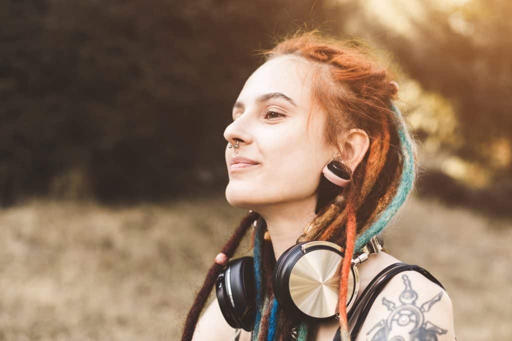 young girl with tattoo and dreadlocks listening to music in the park.