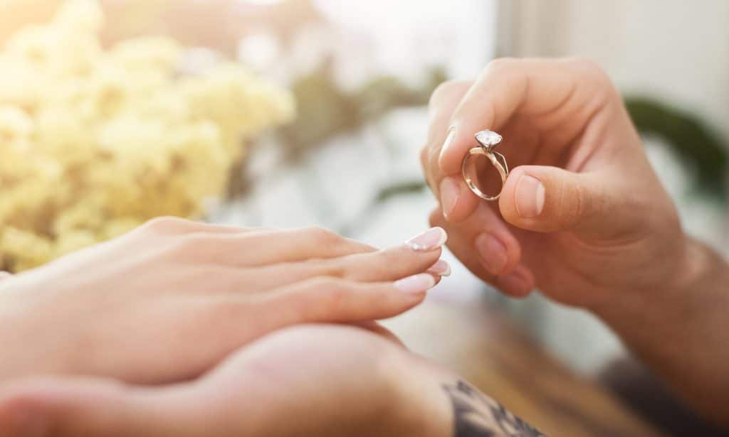 She said YES. Man putting on his girlfriends finger engagement ring, sitting on romantic dinner at cafe. Wedding proposal concept, copy space