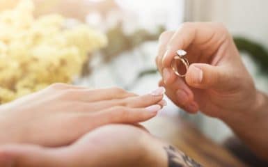 She said YES. Man putting on his girlfriends finger engagement ring, sitting on romantic dinner at cafe. Wedding proposal concept, copy space