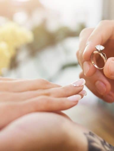 She said YES. Man putting on his girlfriends finger engagement ring, sitting on romantic dinner at cafe. Wedding proposal concept, copy space