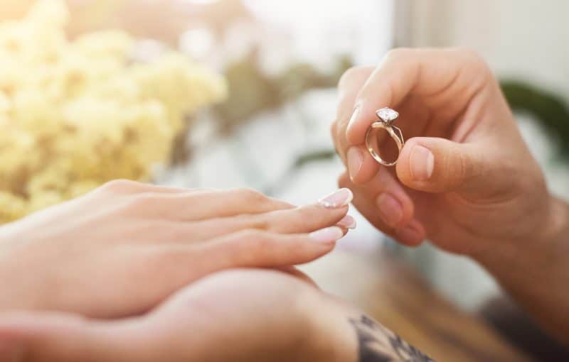 She said YES. Man putting on his girlfriends finger engagement ring, sitting on romantic dinner at cafe. Wedding proposal concept, copy space